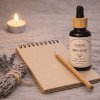 Devote, essential oil blend for love and connection, bottle beside a pen and notebook, ritual styling, label visible Devote, essential oil blend for love and connection, bottle beside a pen and notebook, ritual styling, label visible, The Magic Apothecary