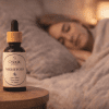 Nightfold oil blend, bedside calm scene Nightfold essential oil blend bottle on a bedside table with a softly blurred person sleeping in the background and warm ambient candlelight.