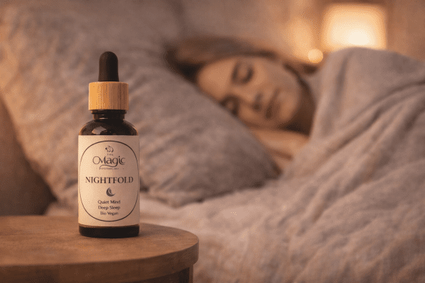 Nightfold oil blend, bedside calm scene Nightfold essential oil blend bottle on a bedside table with a softly blurred person sleeping in the background and warm ambient candlelight.